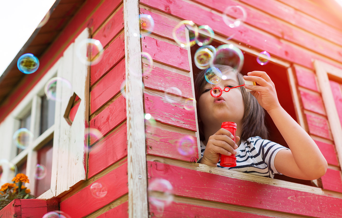 Kind pustet Seifenblasen aus einem spielhaus aus Holz