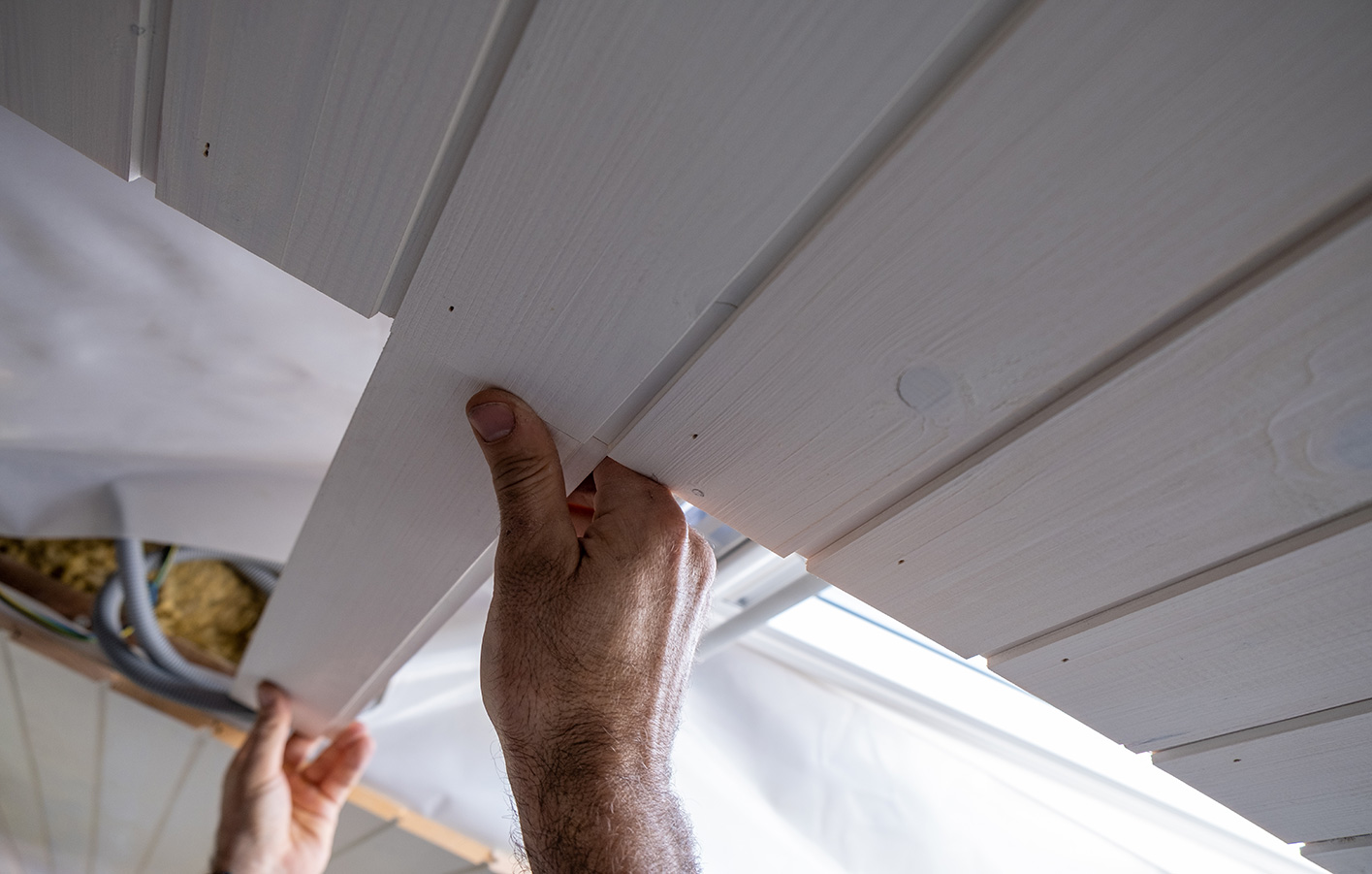Paneele für Wand und Decke anbringen lassen beim Holzmarkt Oetjen Mann befestigt Holzpaneele an einer dachschraegen Decke